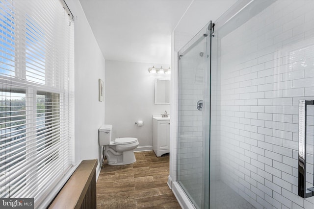 full bath with baseboards, toilet, vanity, wood finished floors, and a stall shower