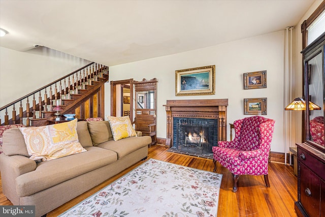 living room with wood-type flooring, baseboards, stairway, and a lit fireplace
