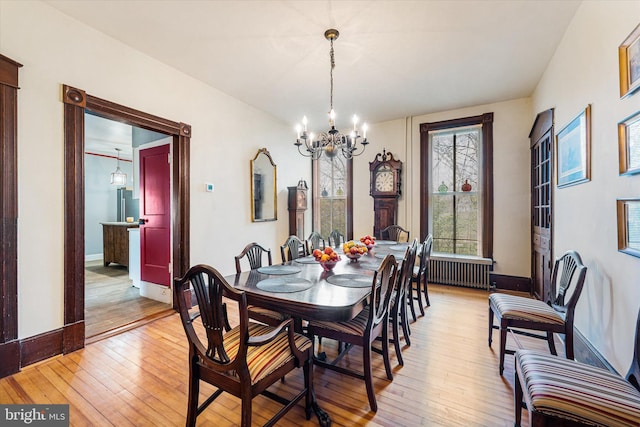 dining area with baseboards, light wood-type flooring, radiator, and a notable chandelier