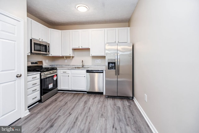kitchen with white cabinetry, stainless steel appliances, light countertops, and a sink