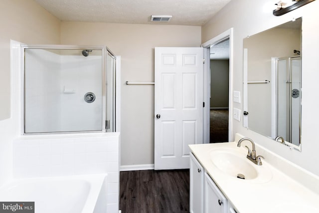 full bath featuring wood finished floors, visible vents, vanity, a garden tub, and a stall shower
