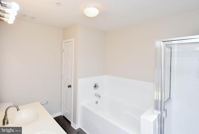 bathroom featuring wood finished floors, visible vents, a sink, baseboards, and a garden tub