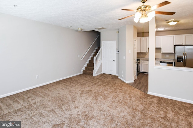 unfurnished living room with stairway, a textured ceiling, ceiling fan, dark carpet, and baseboards