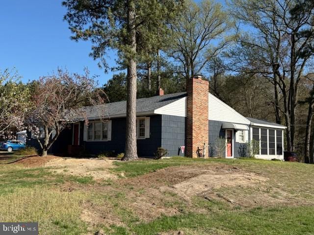 view of property exterior featuring a lawn, a chimney, and a sunroom