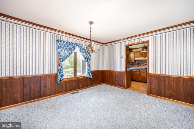unfurnished dining area featuring an inviting chandelier, ornamental molding, wainscoting, and wooden walls