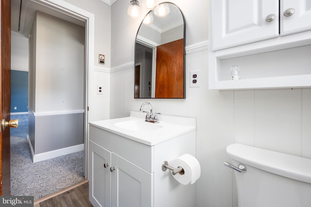 half bath featuring vanity, crown molding, wood finished floors, and toilet