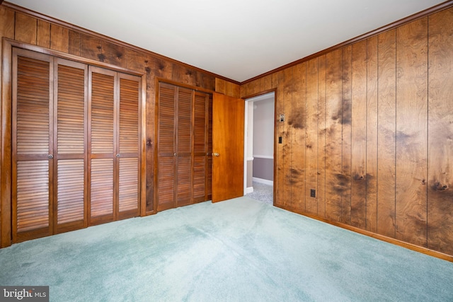 unfurnished bedroom featuring carpet floors, wooden walls, crown molding, and multiple closets