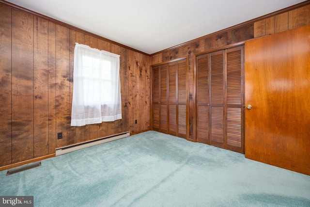 unfurnished bedroom featuring visible vents, wood walls, a baseboard heating unit, two closets, and carpet flooring