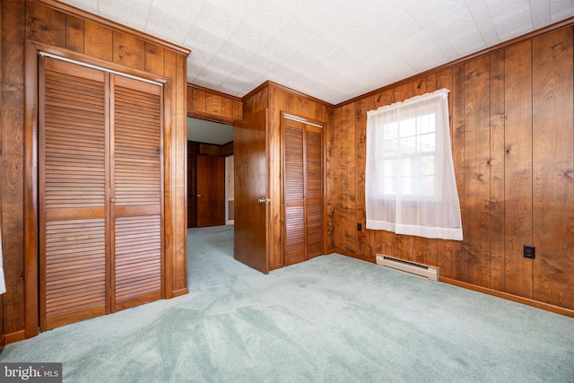 unfurnished bedroom with carpet flooring, wood walls, a baseboard heating unit, and two closets