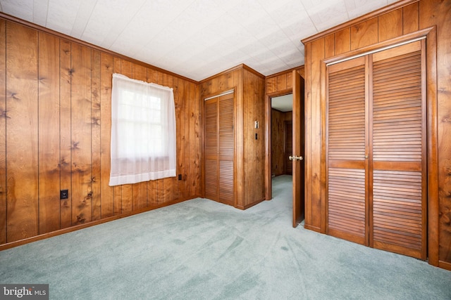 unfurnished bedroom with carpet floors, wood walls, and two closets