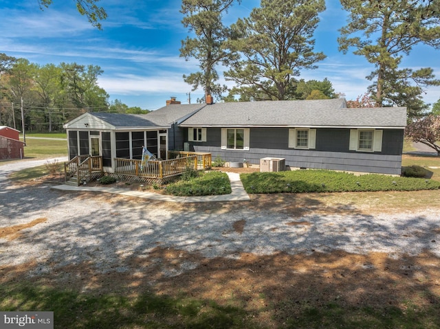 ranch-style home featuring central AC, a wooden deck, a shingled roof, and a sunroom