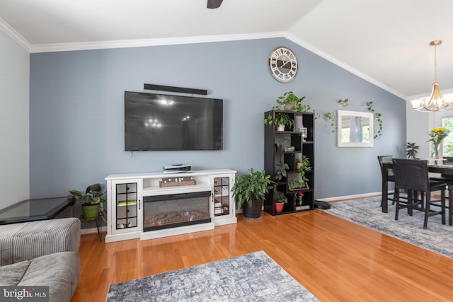 living area featuring vaulted ceiling, baseboards, ceiling fan with notable chandelier, wood finished floors, and ornamental molding
