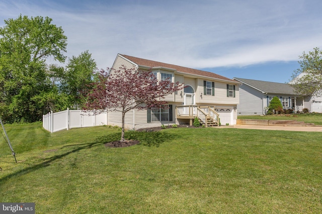 split foyer home featuring concrete driveway, an attached garage, fence, and a front lawn