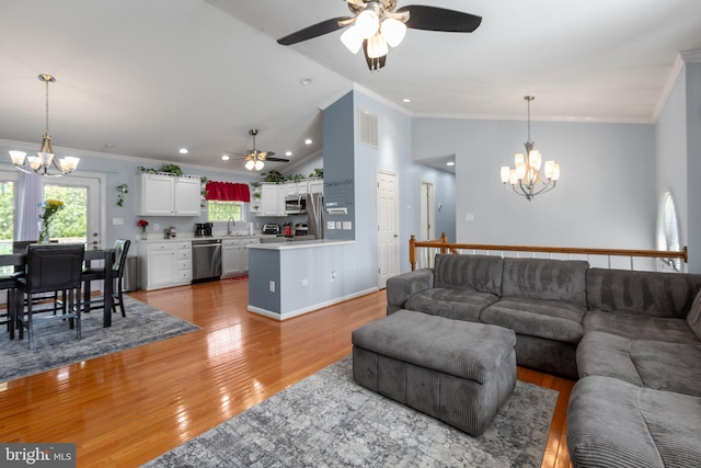 living room with ceiling fan with notable chandelier, vaulted ceiling, light wood-style flooring, and crown molding