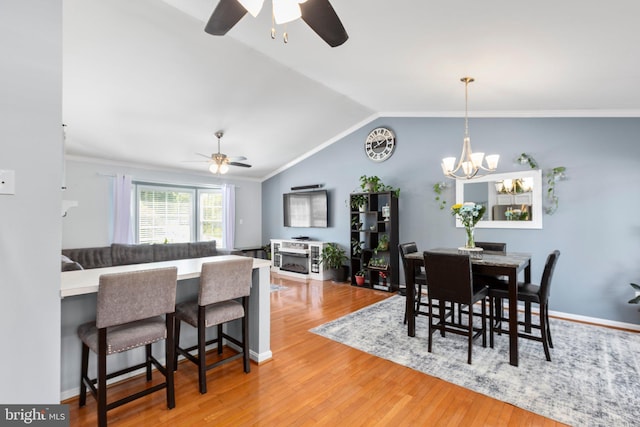 dining area featuring ceiling fan with notable chandelier, vaulted ceiling, wood finished floors, and ornamental molding