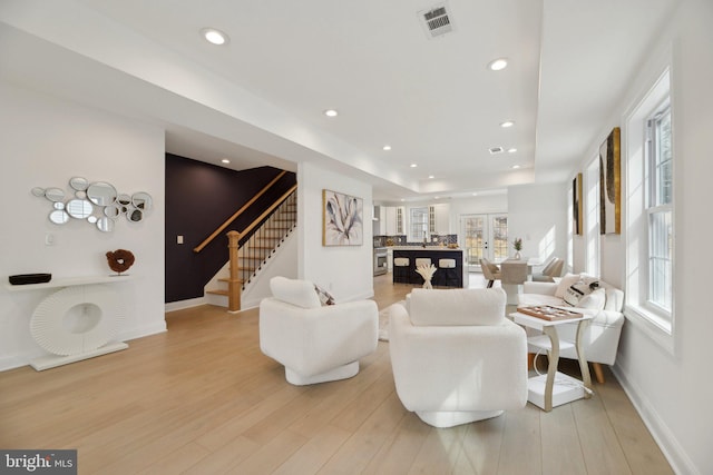 living room with light wood-style flooring, recessed lighting, visible vents, and stairs