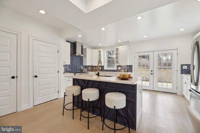 kitchen featuring light wood-style floors, a kitchen bar, wall chimney range hood, white cabinets, and a sink