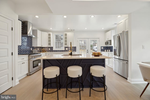 kitchen with light countertops, appliances with stainless steel finishes, wall chimney exhaust hood, and a breakfast bar area