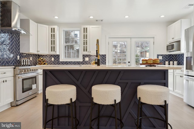 kitchen with a breakfast bar area, appliances with stainless steel finishes, wall chimney exhaust hood, and white cabinets