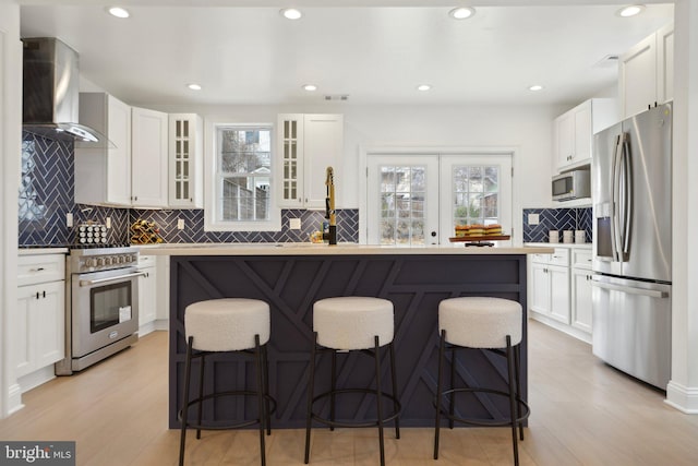 kitchen with stainless steel appliances, a kitchen island, a breakfast bar, and wall chimney range hood