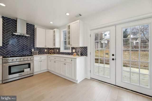 kitchen with light wood-type flooring, visible vents, wall chimney exhaust hood, decorative backsplash, and stainless steel range
