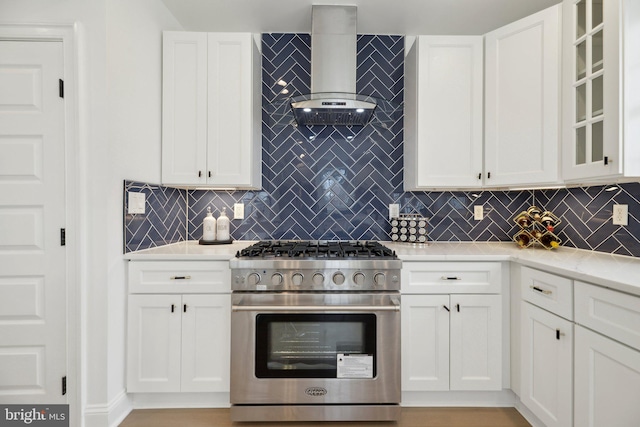 kitchen featuring high end stainless steel range, glass insert cabinets, white cabinets, and wall chimney exhaust hood