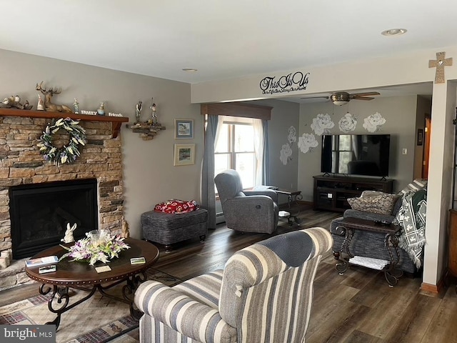 living area featuring a ceiling fan, a baseboard heating unit, a stone fireplace, and wood finished floors