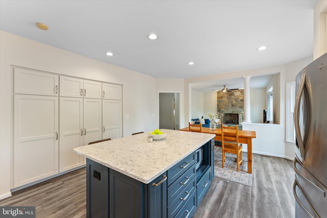kitchen featuring white cabinetry, wood finished floors, a stone fireplace, and freestanding refrigerator