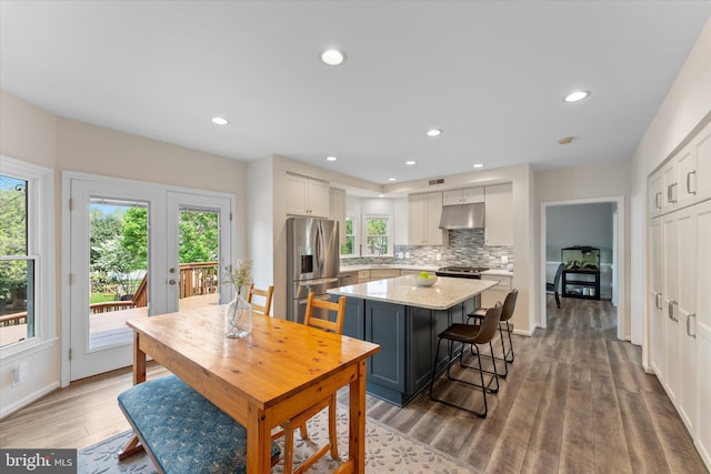kitchen with wood finished floors, decorative backsplash, stainless steel appliances, under cabinet range hood, and a center island