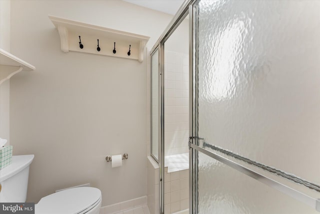 bathroom with toilet, a stall shower, and baseboards