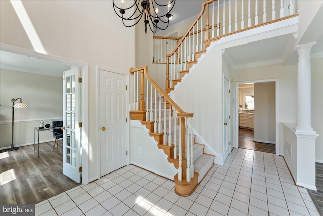 staircase featuring decorative columns, ornamental molding, tile patterned flooring, and a high ceiling