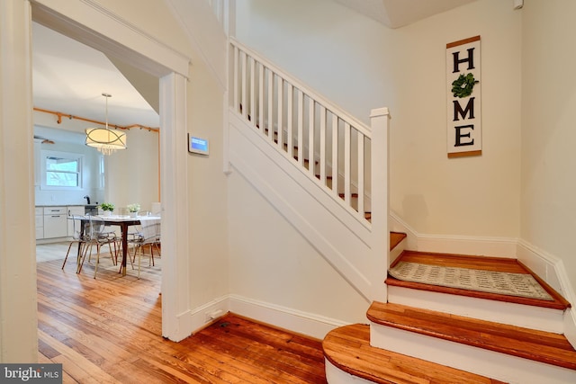 staircase featuring baseboards, an inviting chandelier, and hardwood / wood-style flooring
