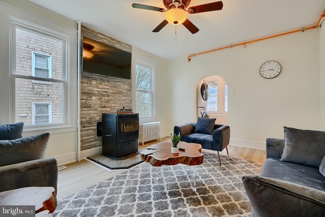living room with ceiling fan, a wood stove, radiator heating unit, wood finished floors, and baseboards