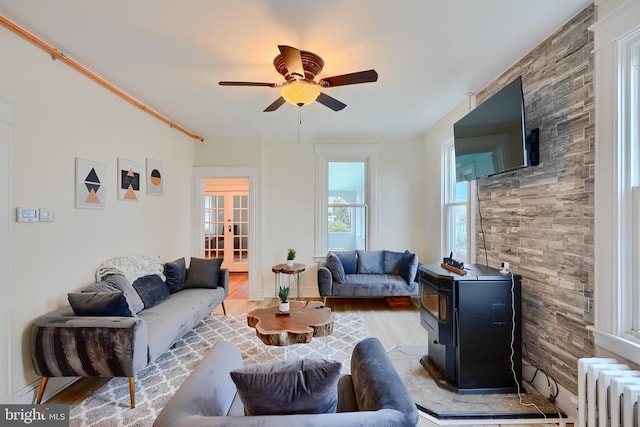 living area featuring a wood stove, ceiling fan, wood finished floors, french doors, and radiator heating unit