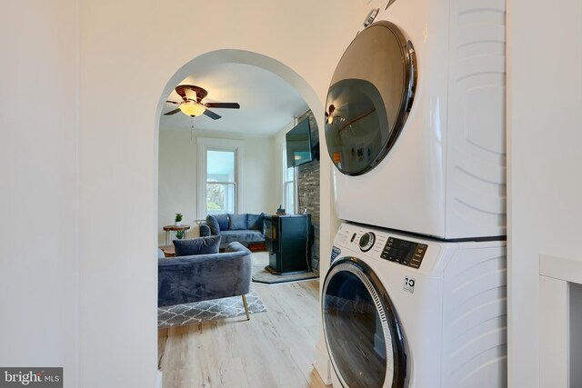 laundry room featuring a ceiling fan, stacked washing maching and dryer, laundry area, arched walkways, and light wood finished floors