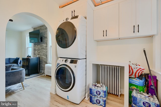 laundry room featuring radiator heating unit, light wood-type flooring, arched walkways, and stacked washer / dryer
