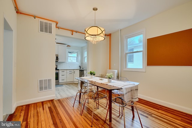 dining space with light wood-style floors, visible vents, and baseboards