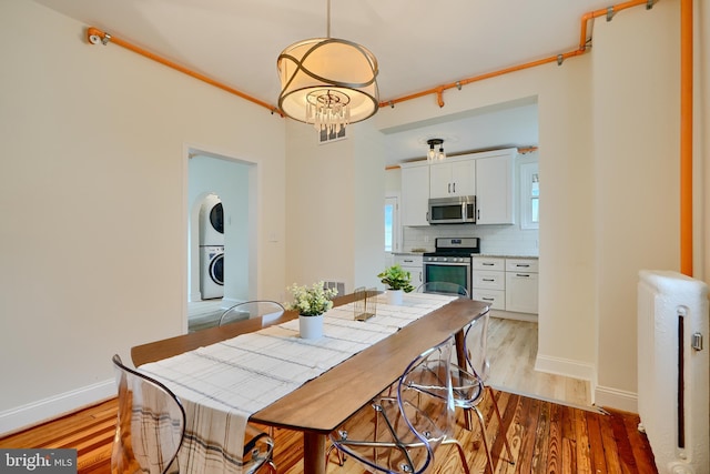 dining room with stacked washer / dryer, an inviting chandelier, baseboards, and light wood-style flooring