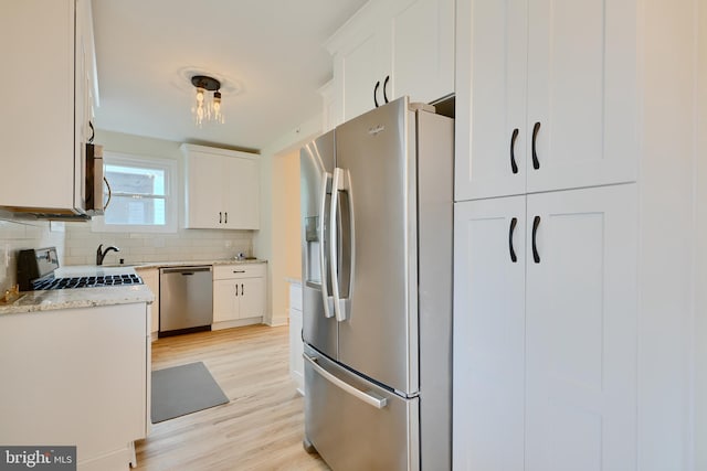 kitchen featuring light wood-type flooring, white cabinetry, decorative backsplash, stainless steel appliances, and a sink