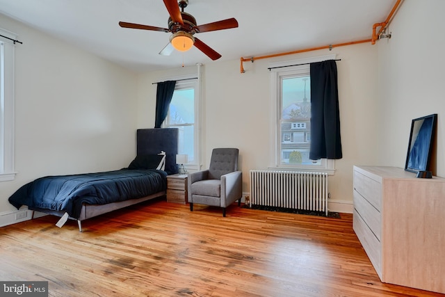 bedroom featuring light wood-style flooring, radiator, baseboards, and a ceiling fan