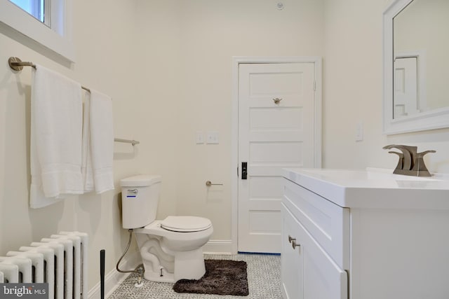 half bath with radiator heating unit, vanity, baseboards, and toilet