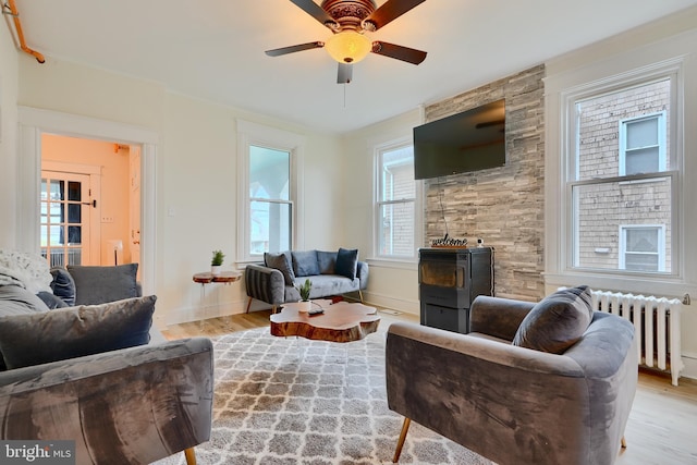 living room featuring baseboards, a wood stove, ceiling fan, radiator, and wood finished floors
