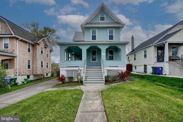 view of front of house with a front yard, a shingled roof, and covered porch