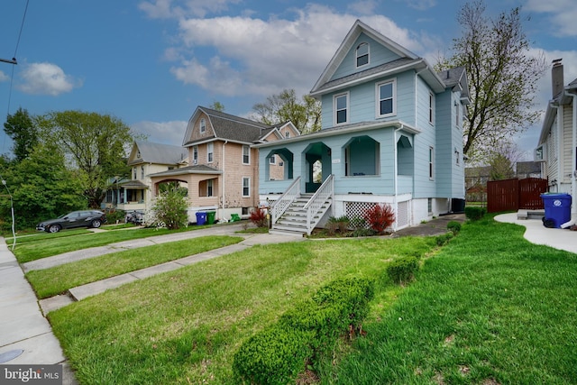 view of front of home with a front yard, roof with shingles, fence, and covered porch