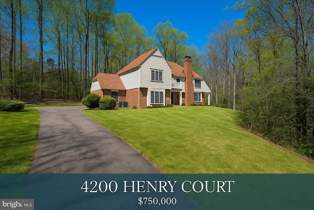 view of front of house featuring brick siding, a balcony, a chimney, and a front lawn