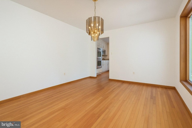 empty room featuring baseboards, a wealth of natural light, a chandelier, and light wood-style floors
