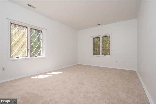 carpeted empty room featuring baseboards, visible vents, and a wealth of natural light