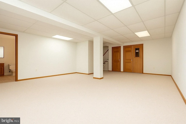 finished basement featuring stairway, a paneled ceiling, light colored carpet, and baseboards