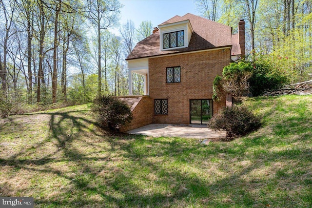 rear view of house with a yard, brick siding, a patio, and a chimney