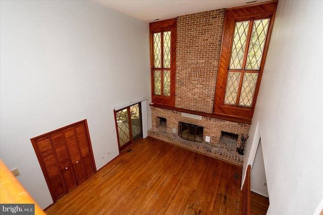 unfurnished living room featuring a brick fireplace, a towering ceiling, and wood finished floors